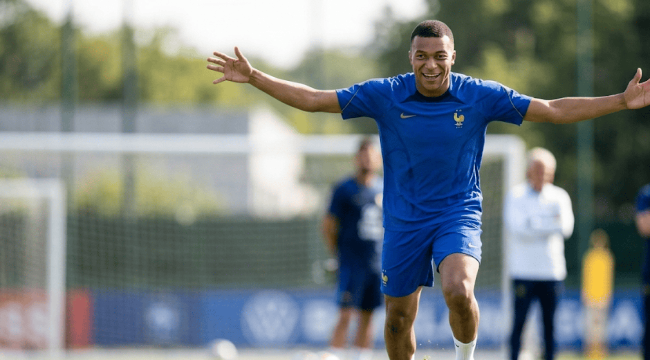 A person wearing the royal blue Kylian Mbappé France FIFA World Cup 2026 athletic T-shirt featuring the golden-brown FFF rooster crest and a deep navy shoulder panel.